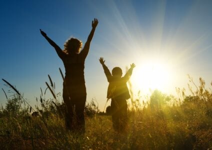 Silhouette of a boy and his mother watching sunrise in the field.