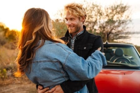 Happy couple smiling and hugging while standing by car outdoors