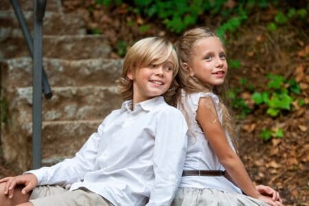 Adorable young girl and boy sitting back to back in park