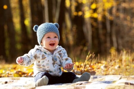 Baby in a funny hat sitting on a blanket in the park