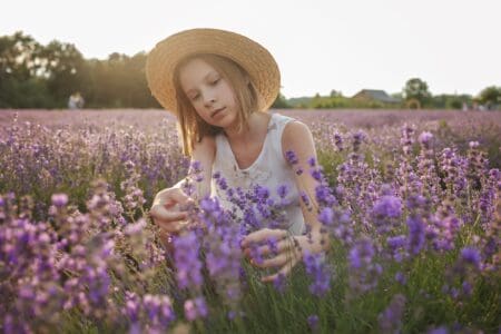 Young girl wearing straw hat sitting in lavender field