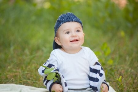 Happy little boy sitting on the grass in the park