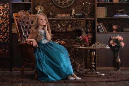 Rich girl wearing fancy gown sitting on chair in vintage room