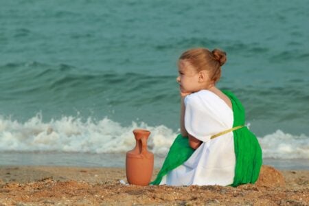 Little Roman girl with amphora sitting on the sea shore.