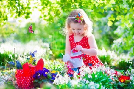 Little girl in a red dress watering flowers in the garden