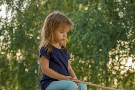 Pretty little girl holding wooden stick over nature background