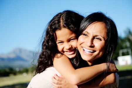 A Hispanic mother playing with her daughter outdoors.