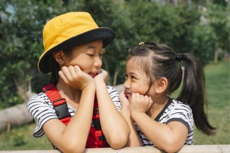 Thai young girls looking at each other while sitting on the bench at green field park.