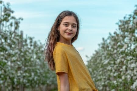 Beautiful brunette curly girl in yellow t-shirt looking at the camera in the garden