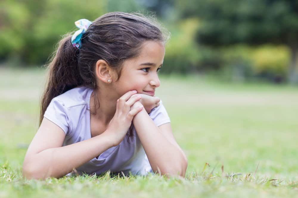 Little girl lying on the grass smiling on a sunny day at the park