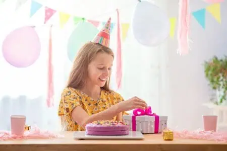 Happy little girl wearing party hat opening her birthday present