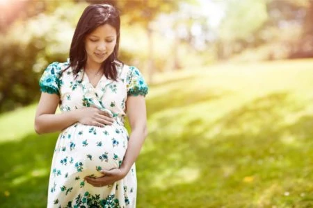 Beautiful Asian mother in a dress holding her belly bump at the park