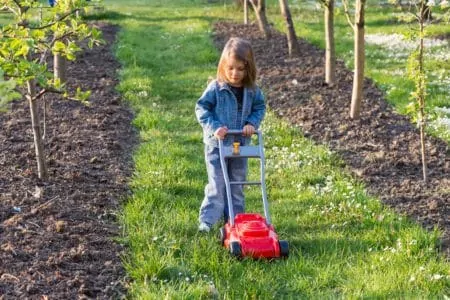 Little girl playing with a toy lawn mower outdoors