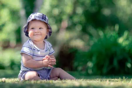 Cute baby sitting on the grass in the garden.