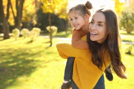 Happy woman giving a piggyback ride to her little daughter in the park