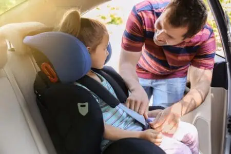 Father buckling his little daughter in car safety seat