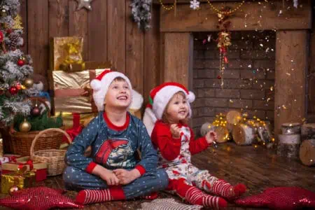 Two kids in pajamas sitting on the living room floor full of christmas decors