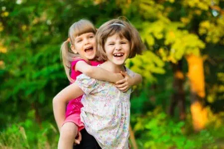 Two cheerful toddler girls playing fly in summer park during sunset