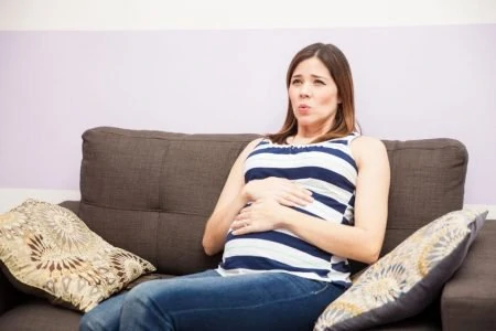 Troubled woman holding her belly bump while sitting on the couch