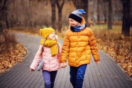 Happy brother and sister walking in the road in autumn park