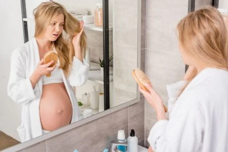 Pregnant woman brushing her hair in front of the mirror