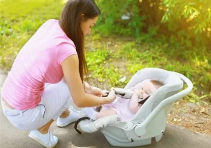 Mom kneeling on the ground while fastening seat belt on her baby's car seat