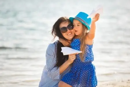 A mother and her daughter launching paper aircrafts at the beach