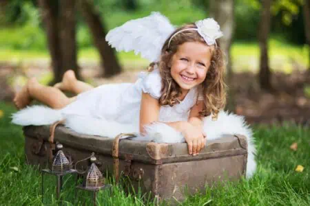 Little girl dressed as an angel lying on a suitcase.