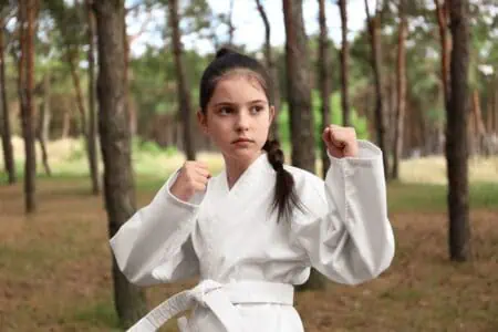 Cute little girl in kimono practicing karate in forest