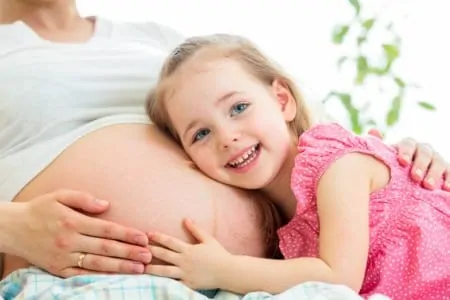 Cute little girl leaning on her mom's pregnant belly