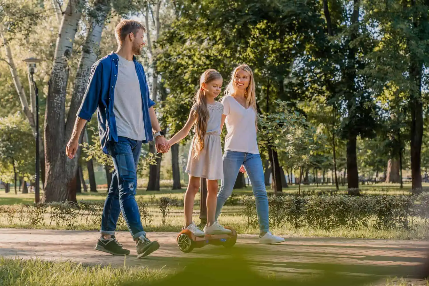 Smiling parents walking in park with their cute little girl riding hoveboard