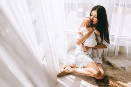 Beautiful mother cuddling her baby while sitting on the floor by the window