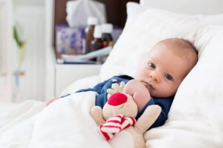 Baby lying in bed with blanket and pillow